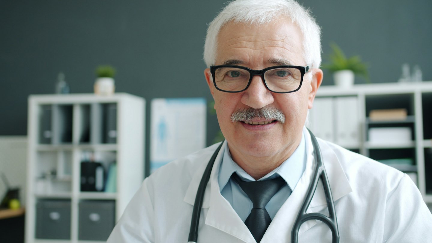 Medico sorridente con occhiali e stetoscopio al collo.