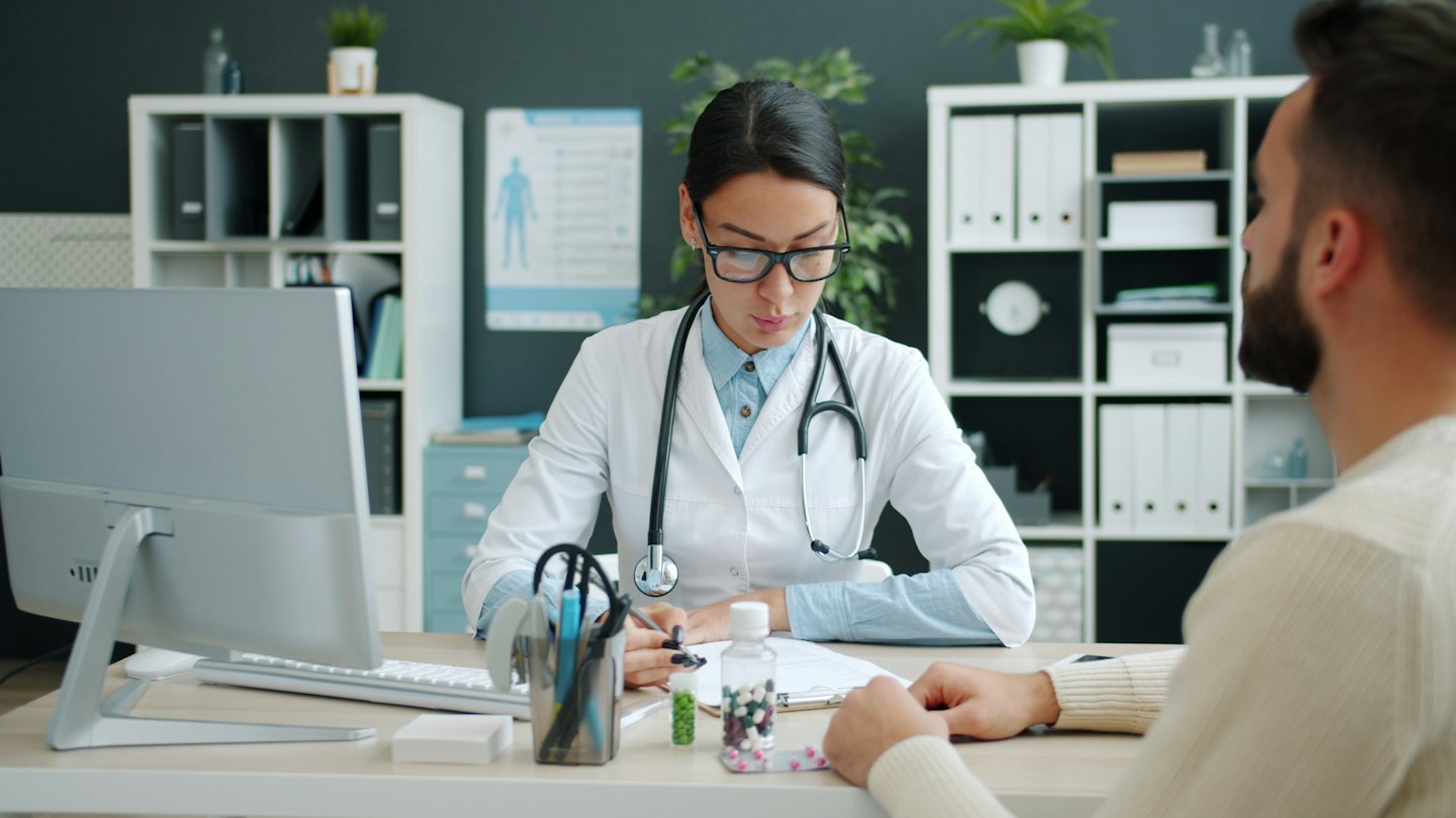 Medico che prende appunti durante una visita medica con un paziente.